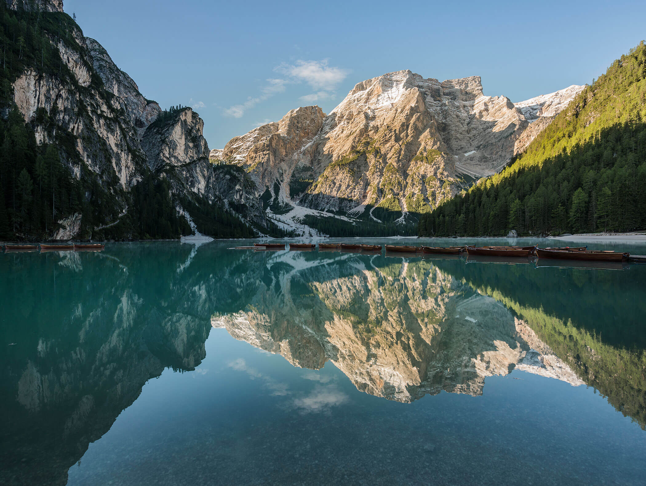 Der Pragser Wildsee mit einigen Holzbooten und die markanten Berggipfel, welche sich im Wasser spiegeln - Hotel Majestic